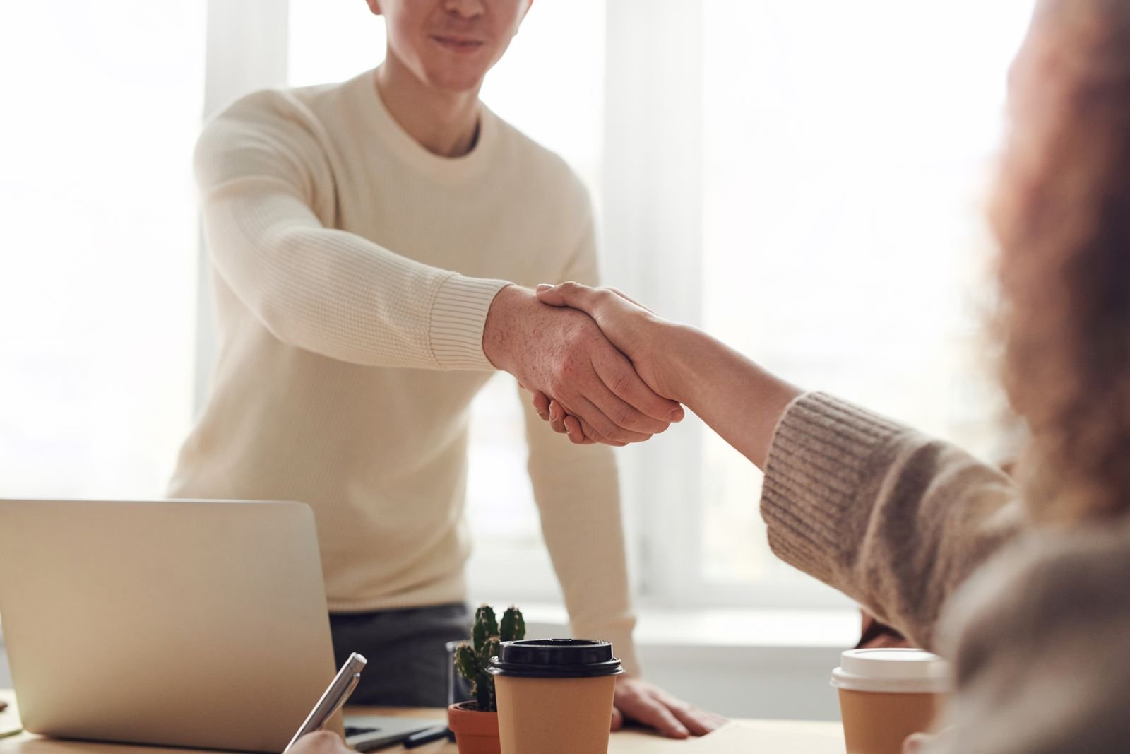 Two people shaking hands over a laptop